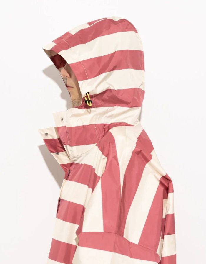 Raincoat Bold Stripes Blush/Sand von VIVI MARI: Langer, wasserdichter Regenmantel im Streifen-Design, oversized geschnitten mit Kapuze, Knopfleiste, Klettverschluss-Manschetten und praktischen Taschen – nachhaltig aus recyceltem Polyester gefertigt.